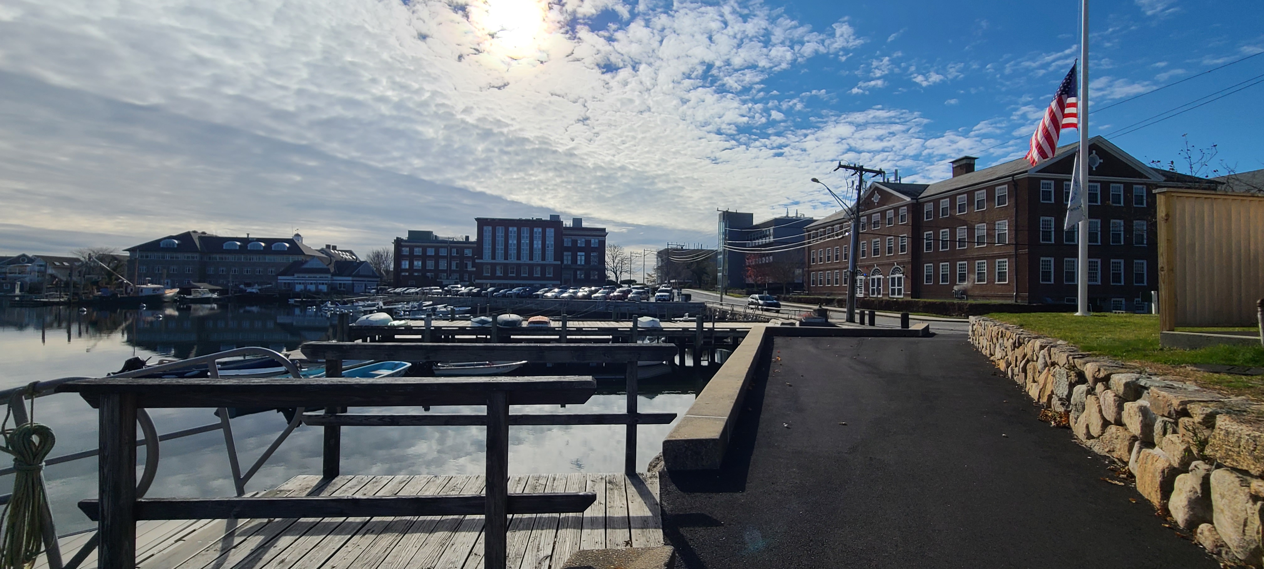 This photo shows an overview of the Marine Biological campus next to the water. The sun is shining above an American flag on the left side of the picture.