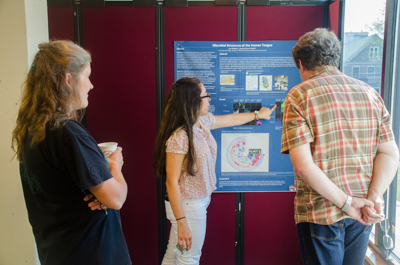 University of Chicago student Isa Alvarez shows her poster to MBL scientist Michael Shribak, right.  She studied the human tongue microbiome with MBL Associate Scientist Jessica Mark Welch, at left.