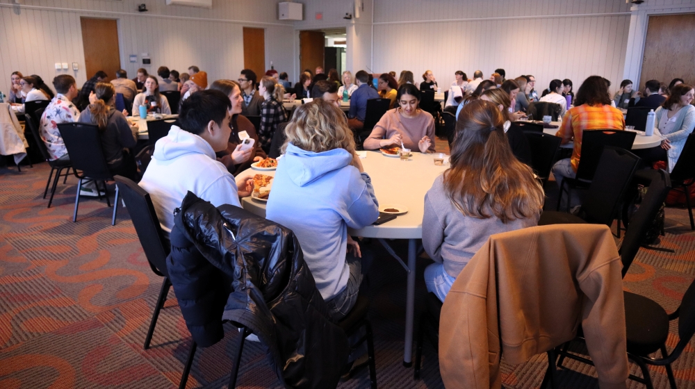 A crowd of people sit at circular tables in a room.