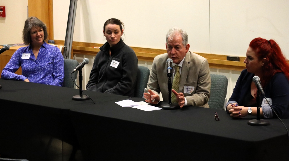 Four people--three women and one man--sit at a table with microphones in front of them.