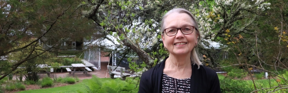 A woman stands outside in front of trees.