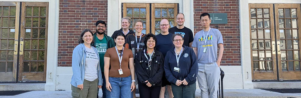 A group of researchers gathers on the steps of a brick building for a cohort photo.