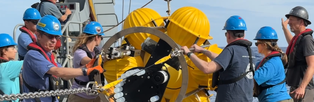This photo shows scientists wearing hard hats and doing oceanic fieldwork on a ship.