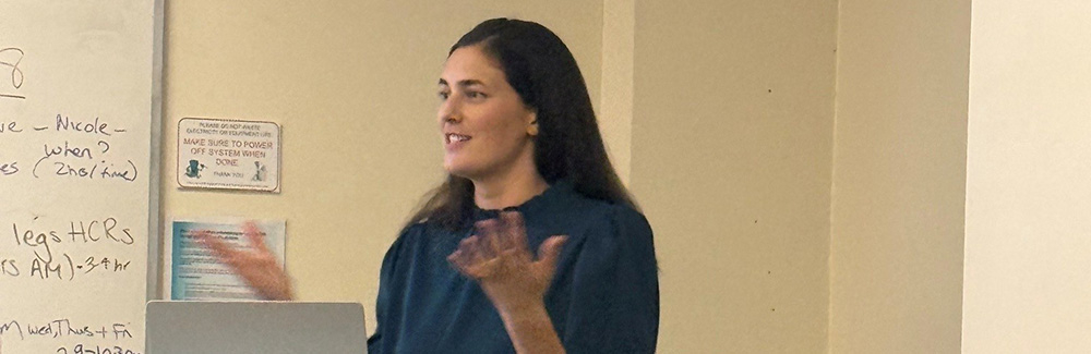 Sam Jones standing in front of podium with computer in front of her and hands up.