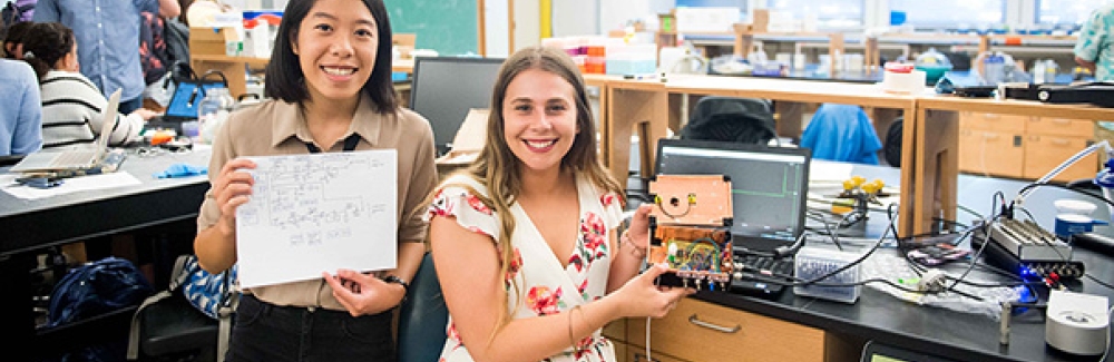 Christina Ford and Alyssa Condie display the plans for and the patch clamp amplifier that they built from scratch in the "Proteins in Action" course. 