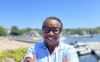 EE Just and Whitman Fellow Sally Seraphin stands with her arms crossed in front of a waterbody on a sunny day.