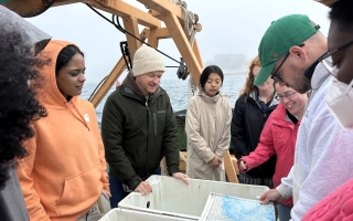 People gather in a circle around empty totes on a boat and look at a map.