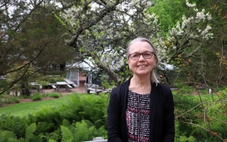 A woman stands outside in front of trees.