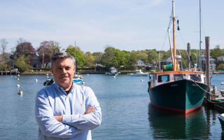 Man in a blue shirt standing and smiling on a dock with a research vessel behind him.