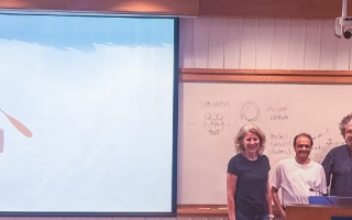 A group of scientists on a stage in front of a documentary screen.