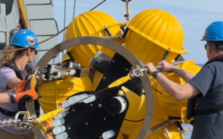 This photo shows scientists wearing hard hats and doing oceanic fieldwork on a ship.
