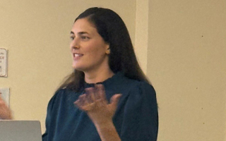 Sam Jones standing in front of podium with computer in front of her and hands up.