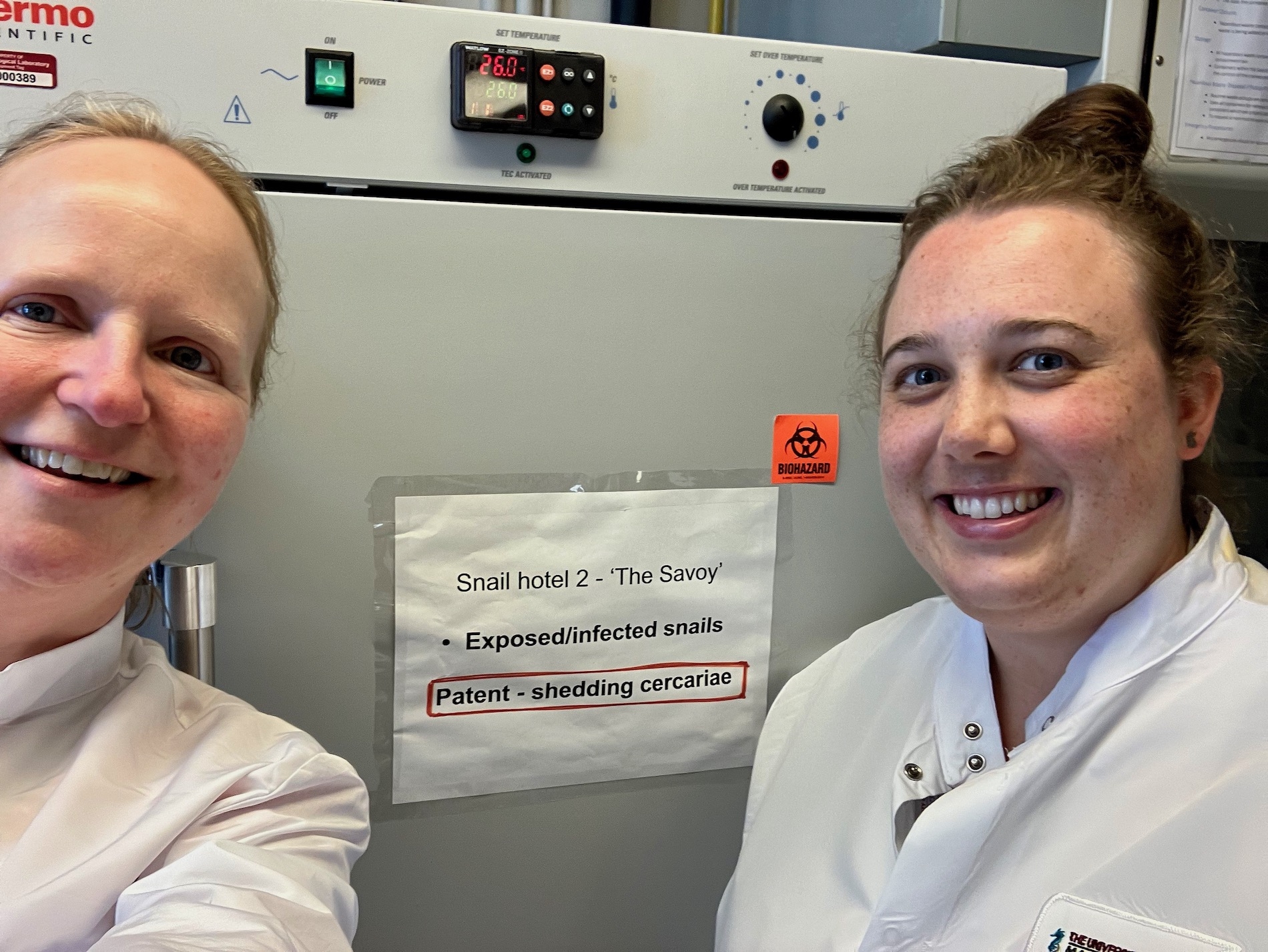 MBL researchers Kate Rawlinson and Teresa Attenborough stand next to an infected snail incubator.