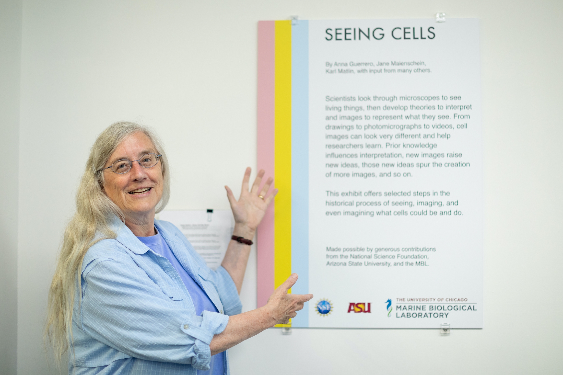 Jane Maienschein stands in front of a sign for the MBL's Seeing Cells exhibit