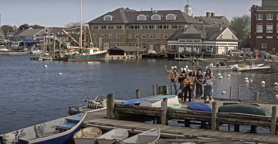 A screenshot from a live YouTube video showing a group of people on the end of a dock