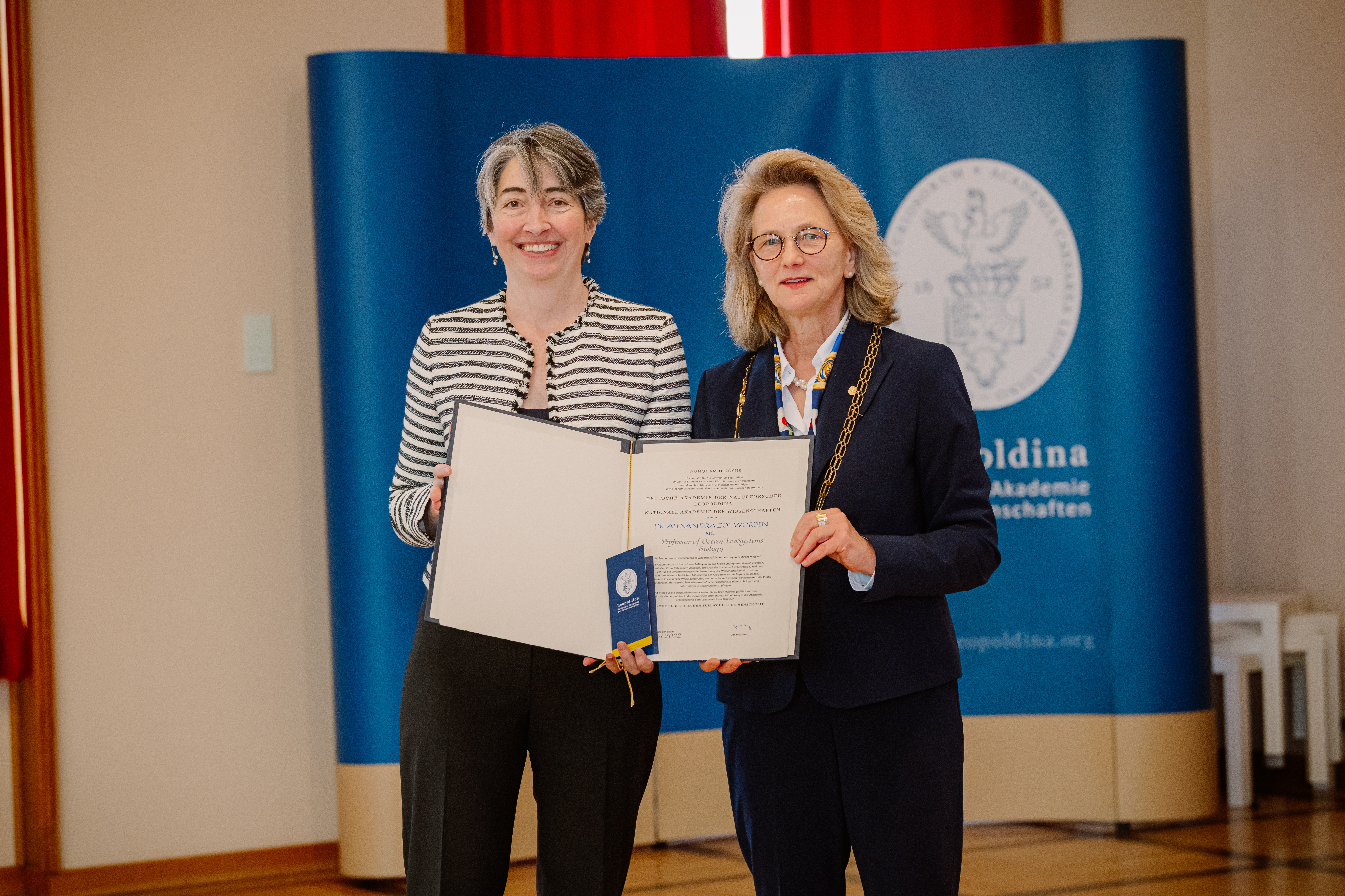 Two women stand next to one another and together hold an open booklet.