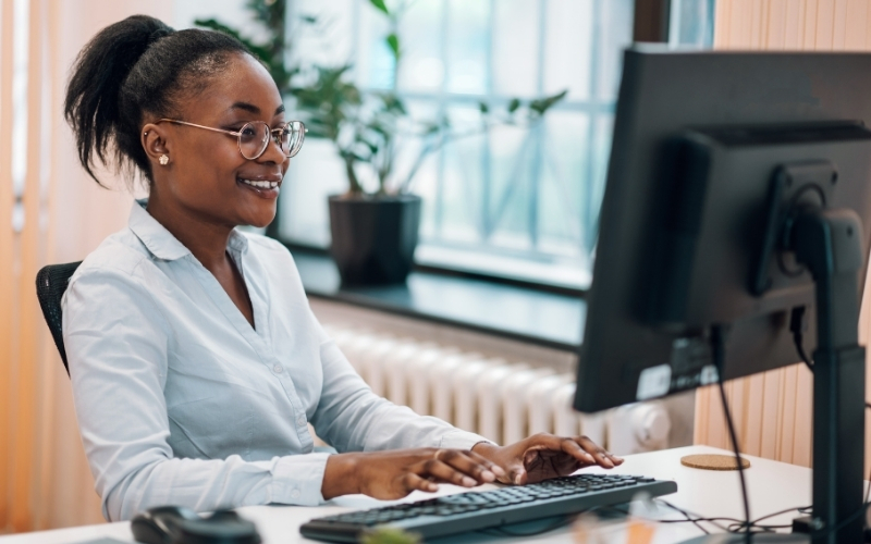 Smiling black woman sitting at a computer.