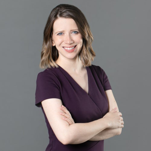 Smiling woman with long dark hair wearing a purple shirt with her arms crossed in front of her.