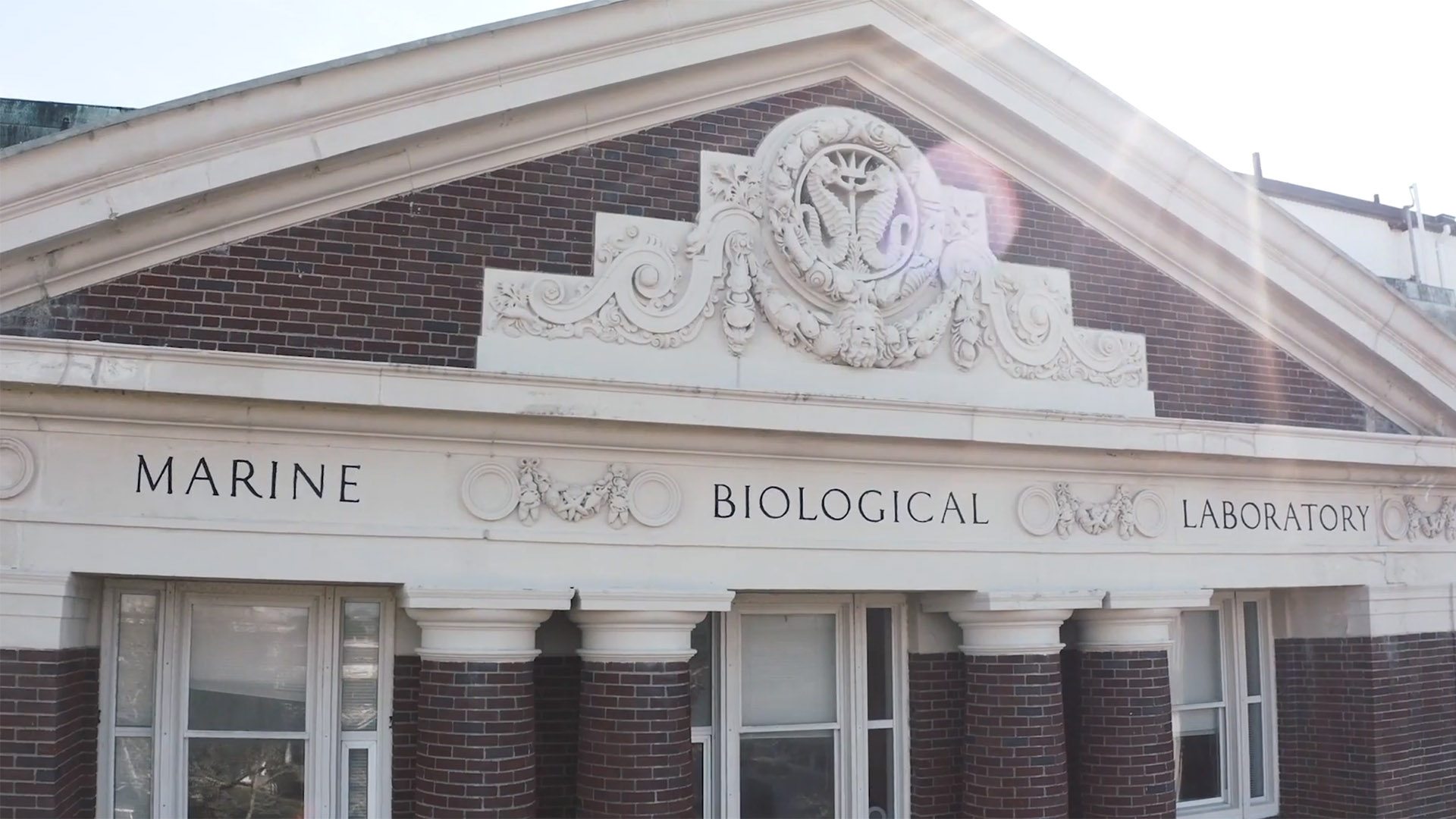 Brick building that says Marine Biological Laboratory on it, with sun behind.