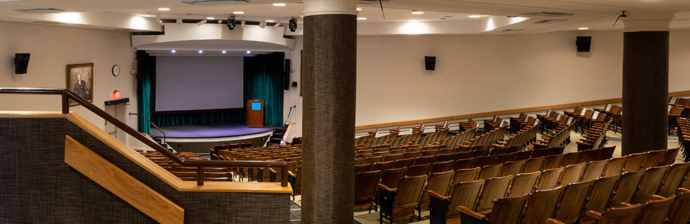 Inside the Clapp Auditorium with screen and rows of seating.