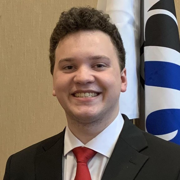 Male presenting person with short dark hair wearing a suit.