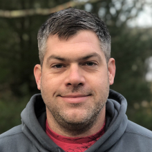 Male presenting person with short dark hair wearing a gray hoodie.