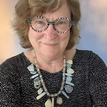 Female presenting person with short brown hair wearing funky glasses and necklace,