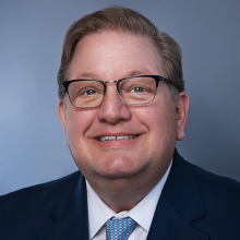 Male presenting person with short dark hair wearing a suit.