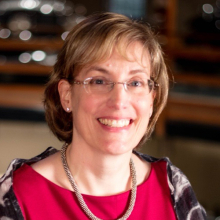 Female presenting person with short blond hair and glasses wearing a red shirt.