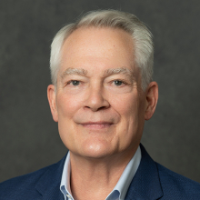 Male presenting person with short gray hair.